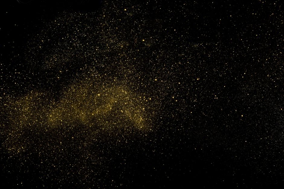 A captivating cosmic scene with golden dust resembling stars against a deep black background.