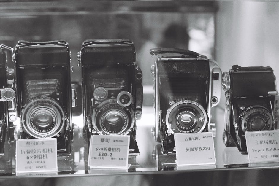 Black and white photo of vintage cameras on display with descriptive signs.