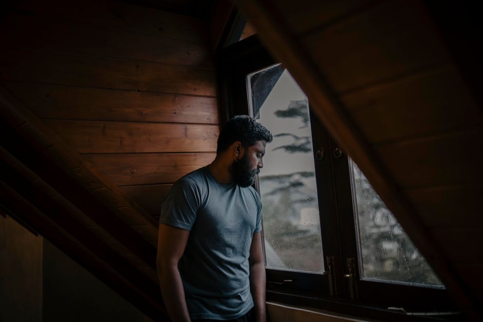 A thoughtful man stands by a window, lost in contemplation, indoors in Sri Lanka.