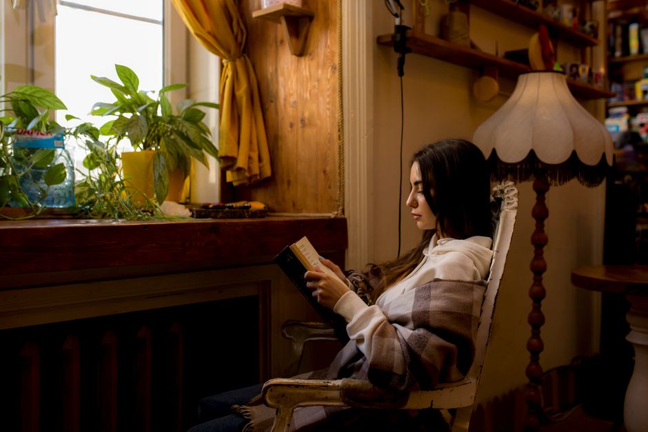 Woman reading in a cozy corner, wrapped in a plaid, under warm lamp light.