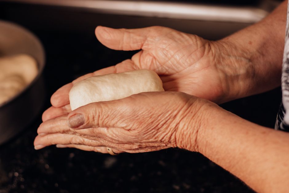 Close-up of senior woman's hands shaping dough in a kitchen setting.
