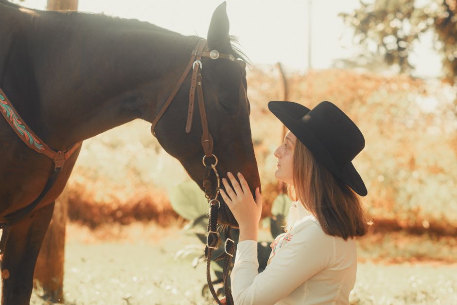 A cowgirl gently connecting with her horse in a sunlit outdoor setting, evoking a serene bond.